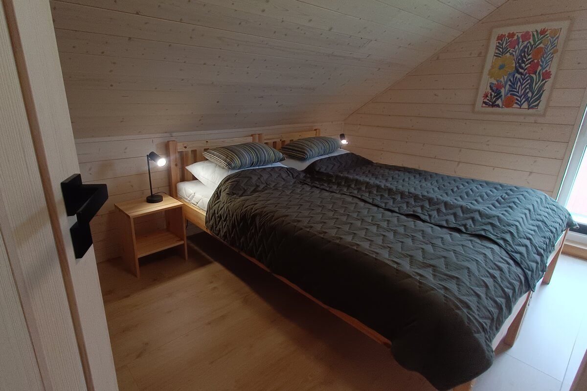 Sypialnia w domku letniskowym – drewniana boazeria, kolorowe poduszki i lampki nocne, przytulne wnętrze idealne na wypoczynek.